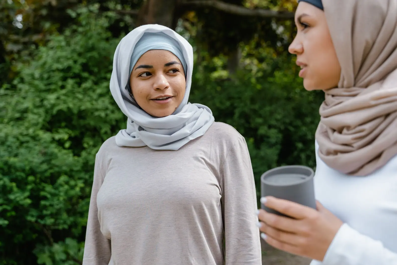 Two women in hijab talking outdoors, one listening with a calm smile